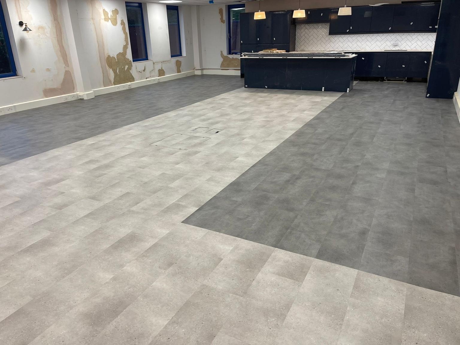 Large-format tile-effect flooring fitted across a commercial kitchen and dining space, with a contrasting darker border set into the lighter field
