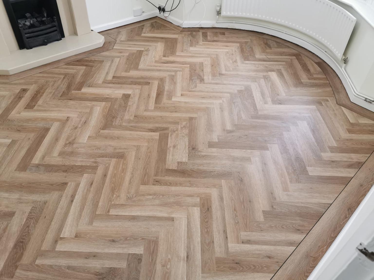 The finished herringbone floor seen across the room, the border sweeping round the curved bay and along the fireplace